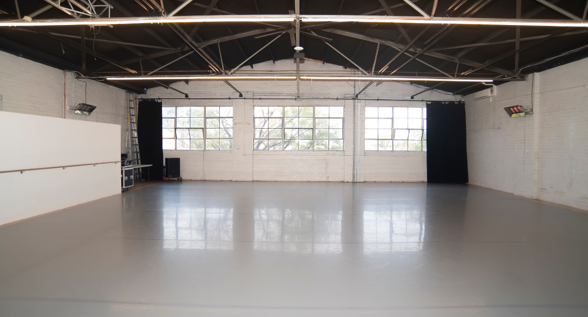 Rehearsal space, North Melbourne. A large light-filled dance studio with grey floors, thin light beams and three large industrial windows.