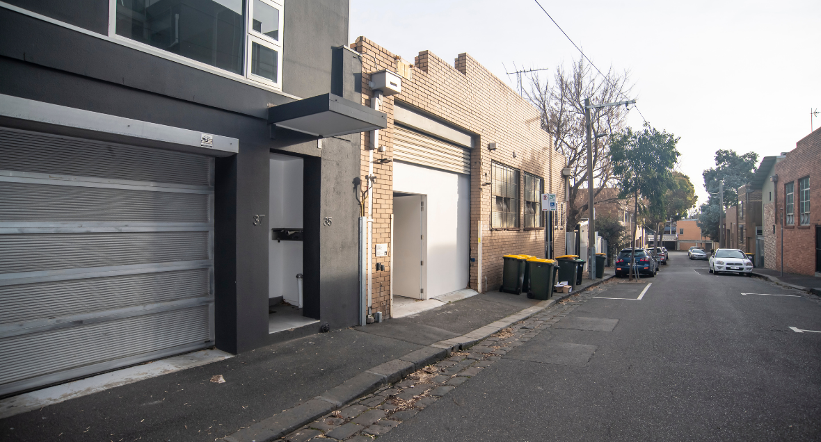 Wheelchair Accessible Rehearsal space, North Melbourne. A large white door and pavement seen from the road. Curb but leads to three rows of cobble stones.