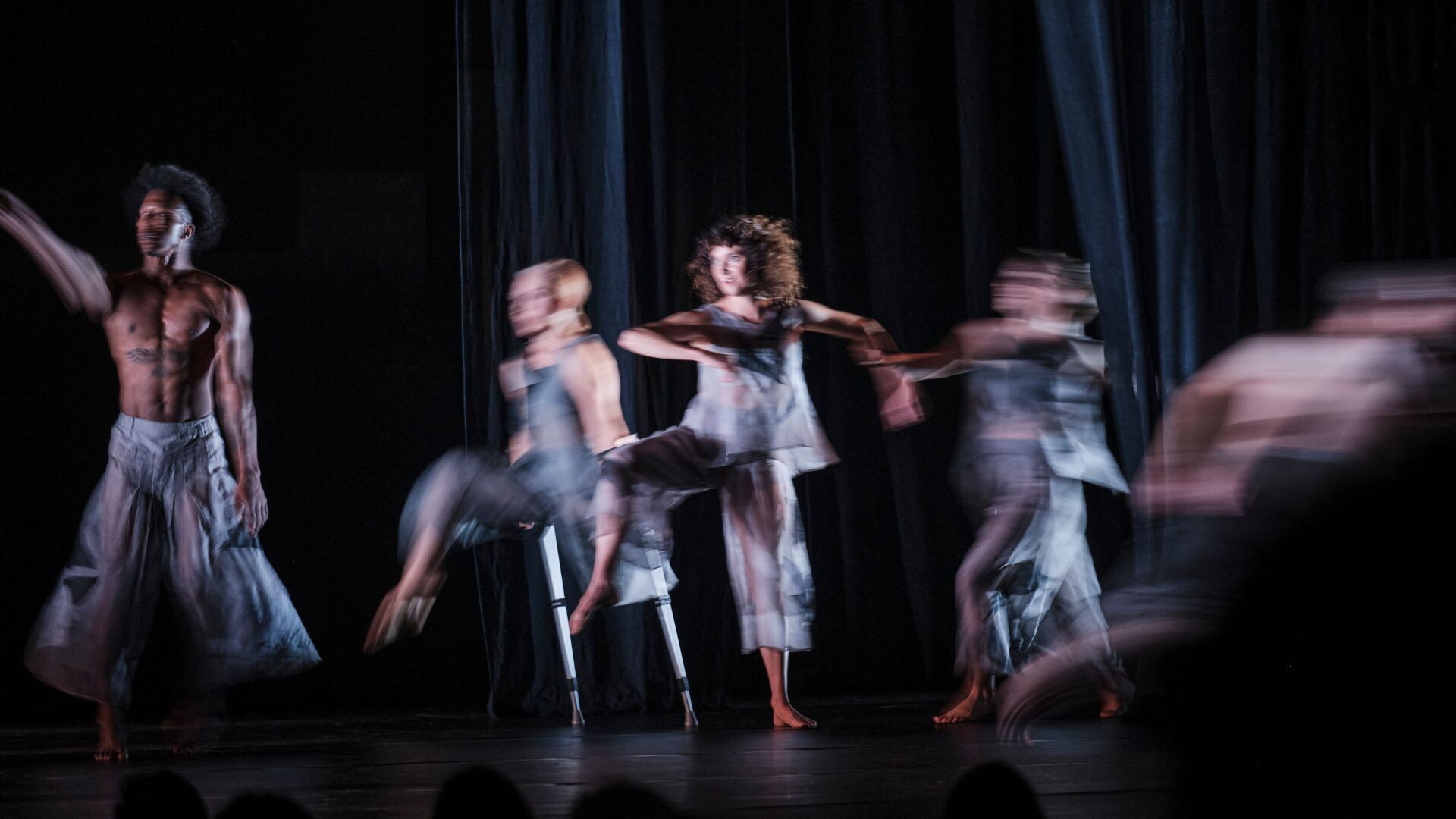 Four blurred figured in silver costumes move on stage
