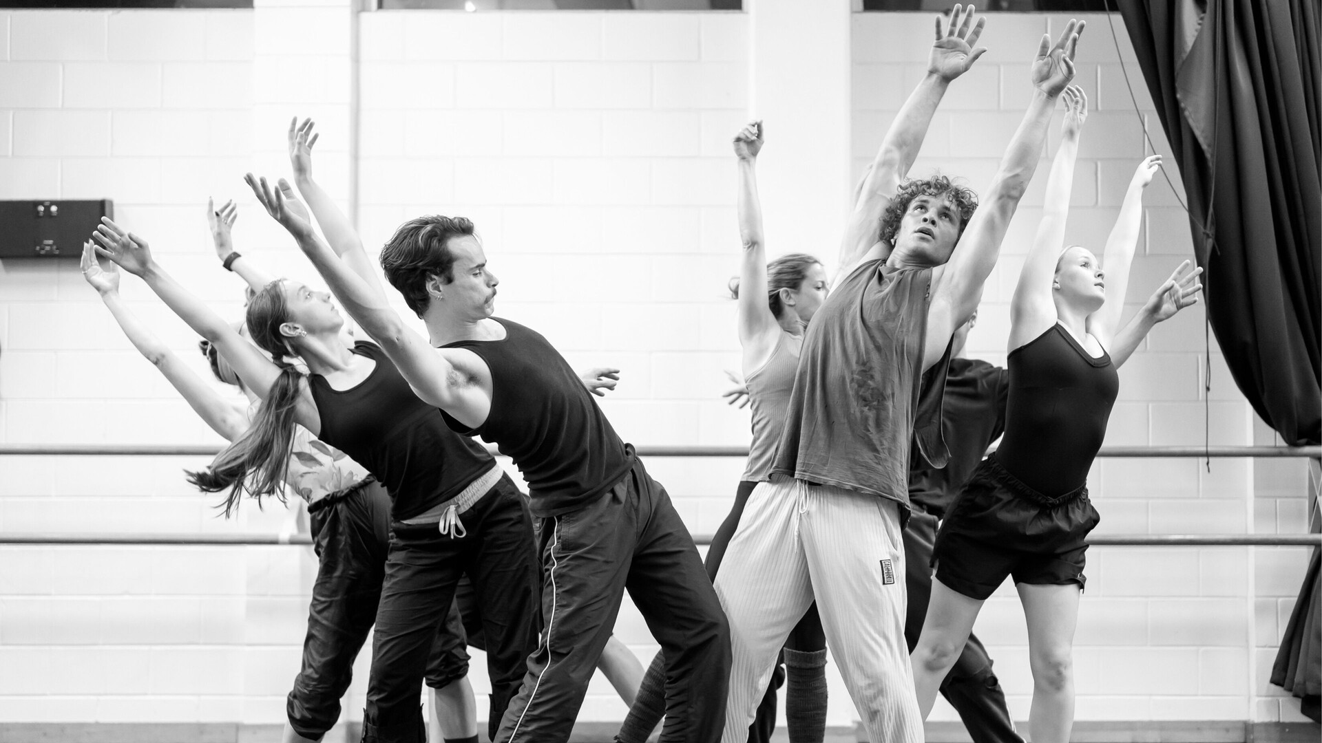 Black and white image of 8 dancers, parted in groups of 4 leaning away from each other, with their arms raised.