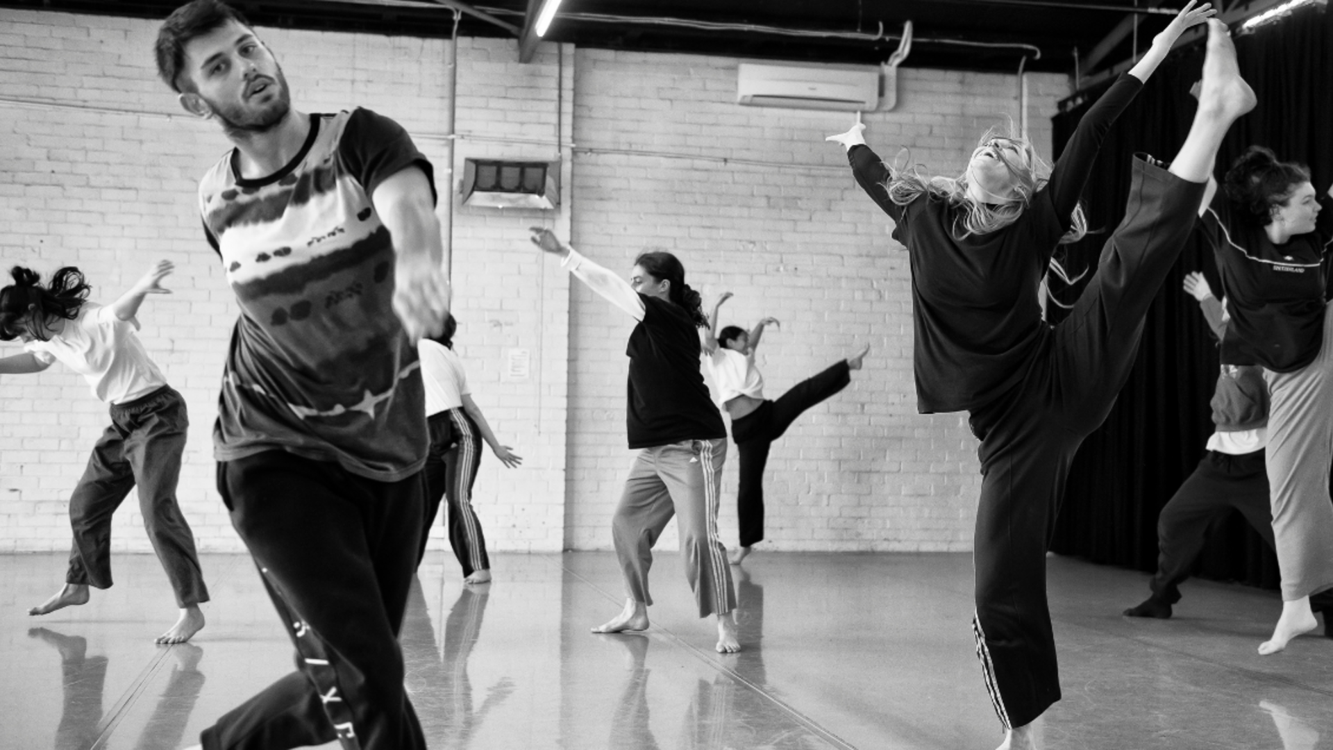 A group of dancers in a light filled studio engaged in improvised movement.