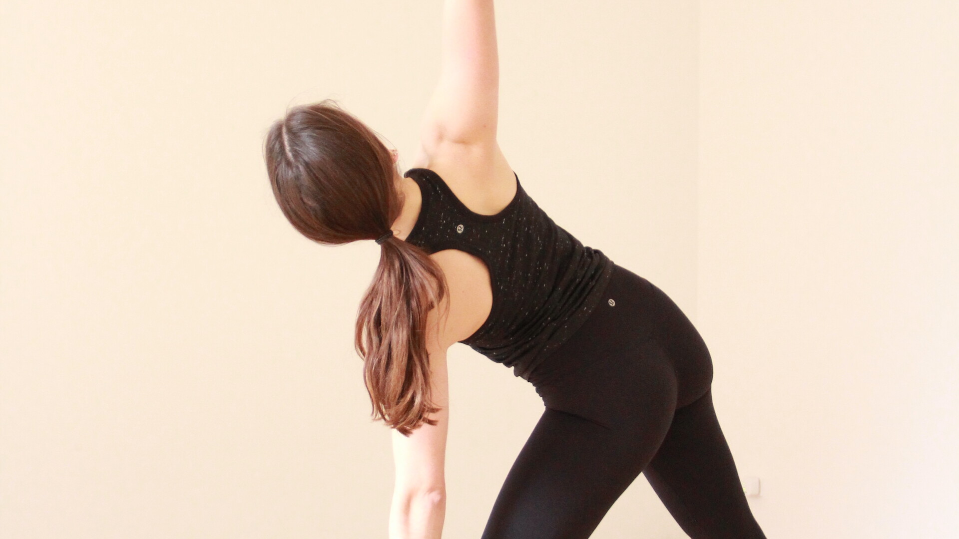 A yoga student in a standing yoga posture, Trikonasana or Triangle pose. She has both feet spread out on her mat and is stretching out to the side, while reaching one arm up and one arm down. She is looking to the sky.