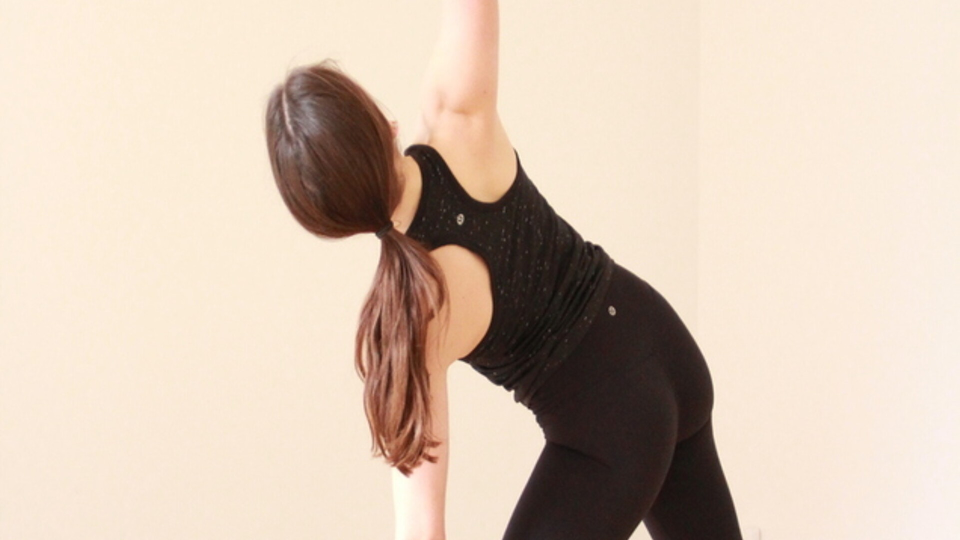 A yoga student in a standing yoga posture, Trikonasana or Triangle pose. She has both feet spread out on her mat and is stretching out to the side, while reaching one arm up and one arm down. She is looking to the sky.