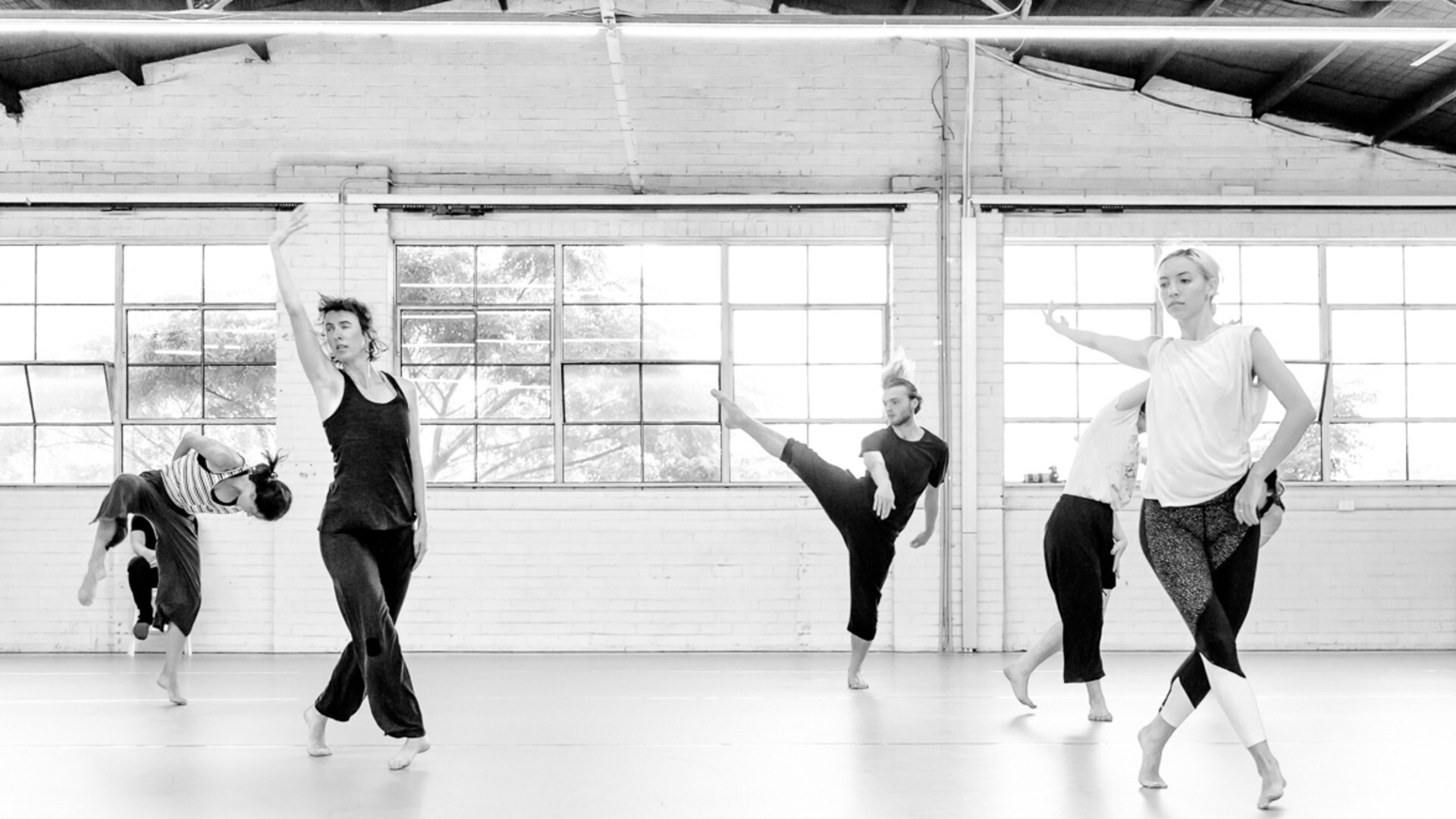 A group of dancers rehearsing in brightly lit studios—each improvising their own movement.