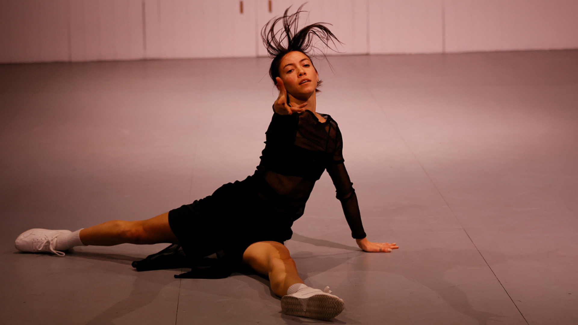 Dancer Tra Mi Dinh performing in Out of Bounds 2022 at Temperance Hall. She is wearing a black shift dress and white sneakers, moving on the floor with an arm outstretched o the audience.