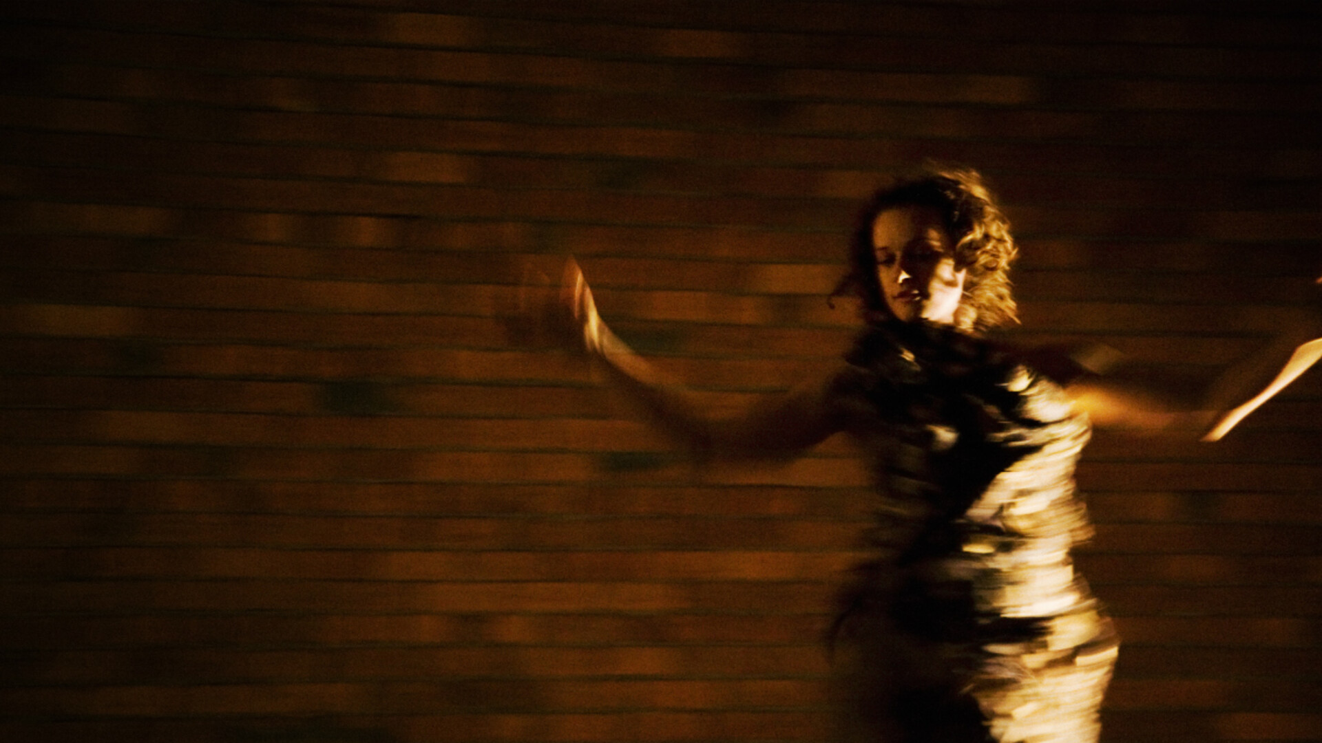 Dancer Carlee Mellow frontlit in a gold dress spinning in front of a brick wall